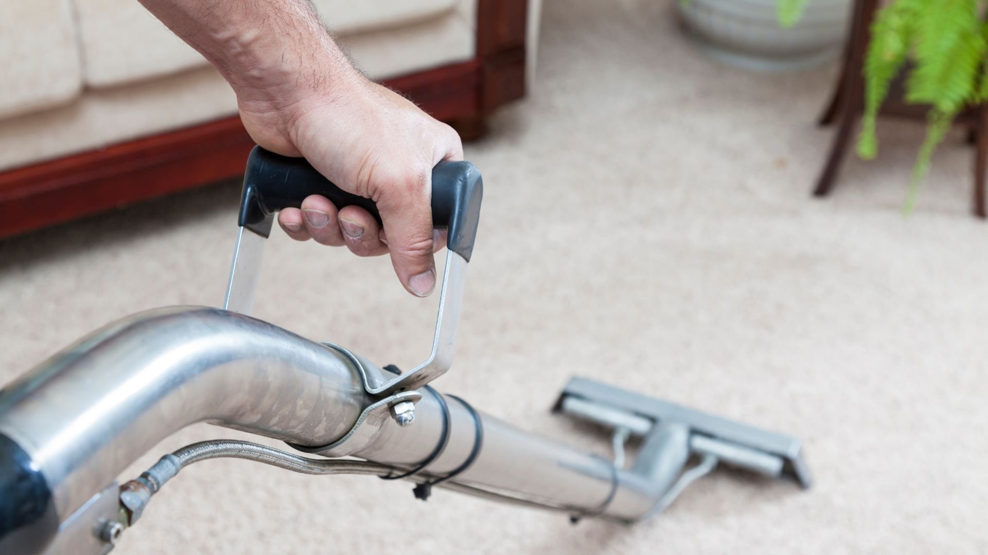 Hand using carpet cleaning vacuum cleaner on light-colored carpet