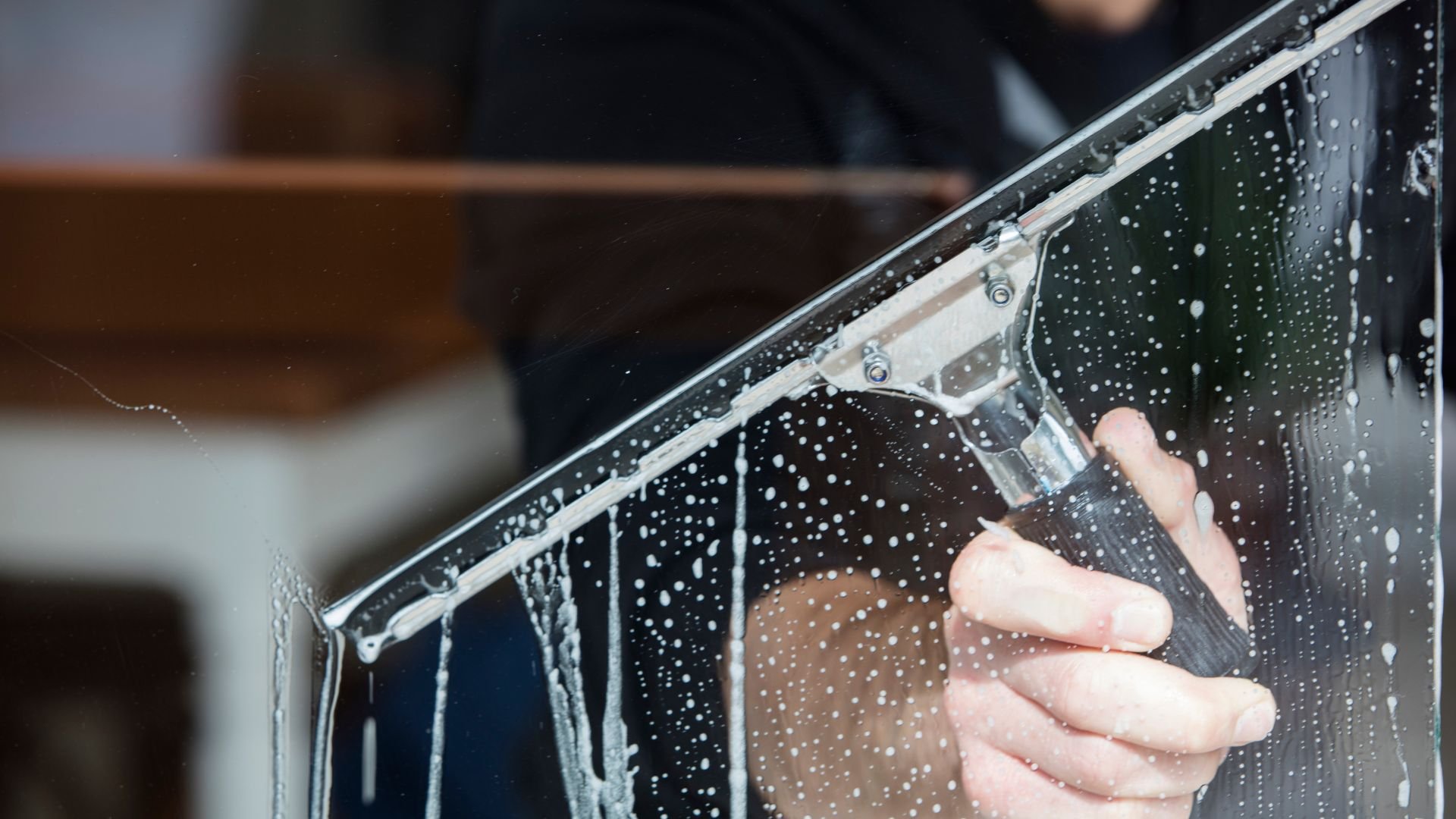 Hand using squeegee to clean wet window with water droplets