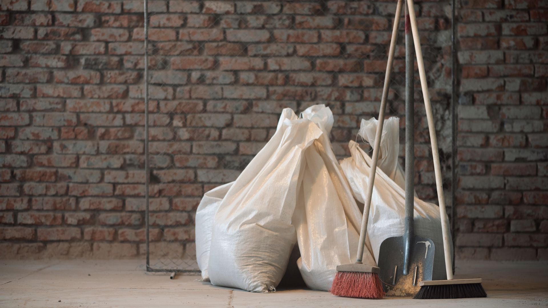 White bags, broom, and dustpan against a brick wall interior