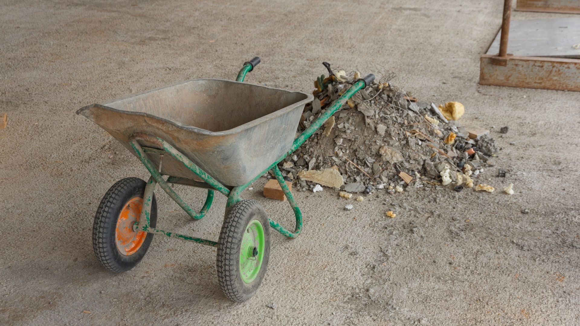 Wheelbarrow with green frame next to pile of construction debris