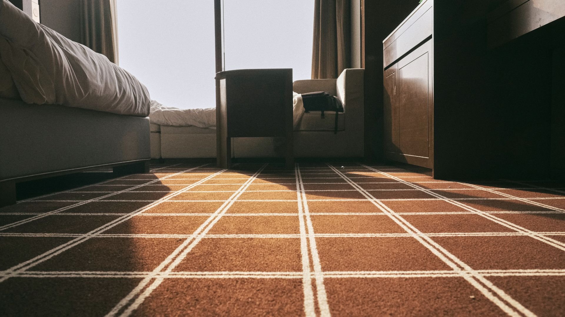Sunlit hotel room with checkered carpet and minimalist furniture